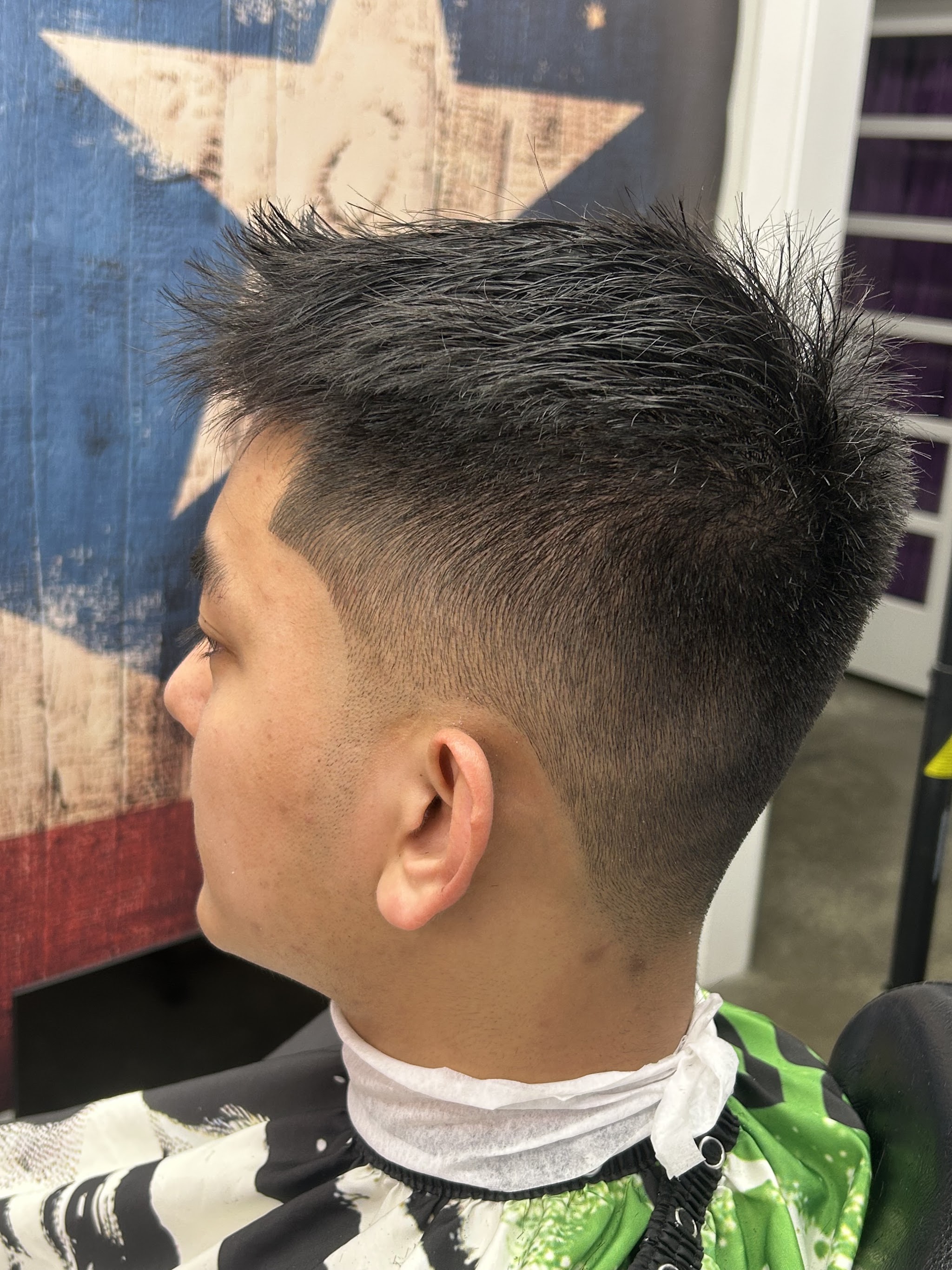 A fresh fade with a textured top, in front of the Puerto Rican flag star on the shop wall