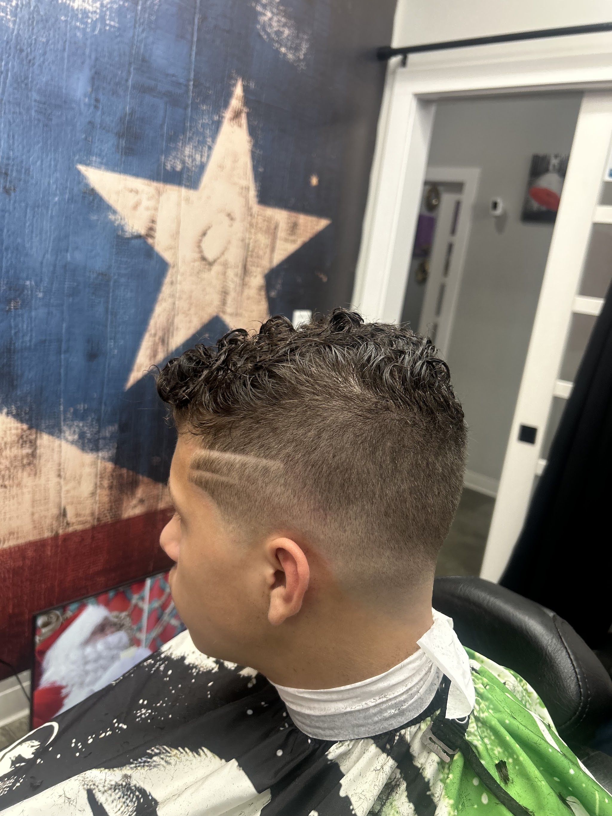 Curly textured cut with a hard line design, in front of the flag wall